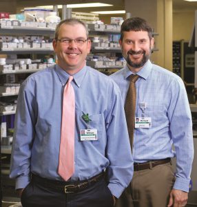 Richard and William posing together at work in a pharmacy.