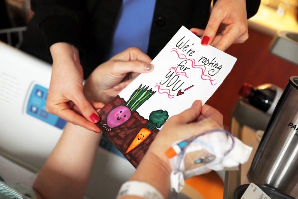 Person giving a handwritten card to a patient that says "We're rooting for you"