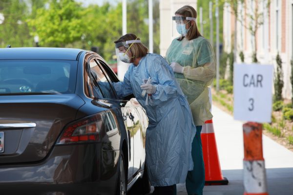 Lexington Medical Center clinicians conduct drive-thru COVID-19 testing in a parking lot for a patient in a black car.