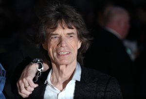 singer Mick Jagger in a black suit and white shirt smiling