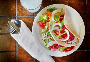 White plate of spicy fish tacos with beet slaw with a rolled napkin of silverware