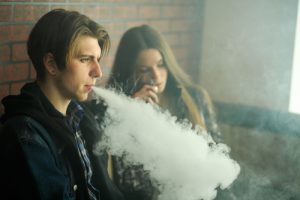 Image of a man and woman sitting on a couch with man blowing out smoke