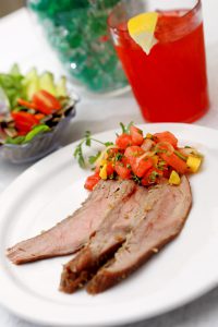 Steak with watermelon-mango chutney on a white plate with cup of red drink