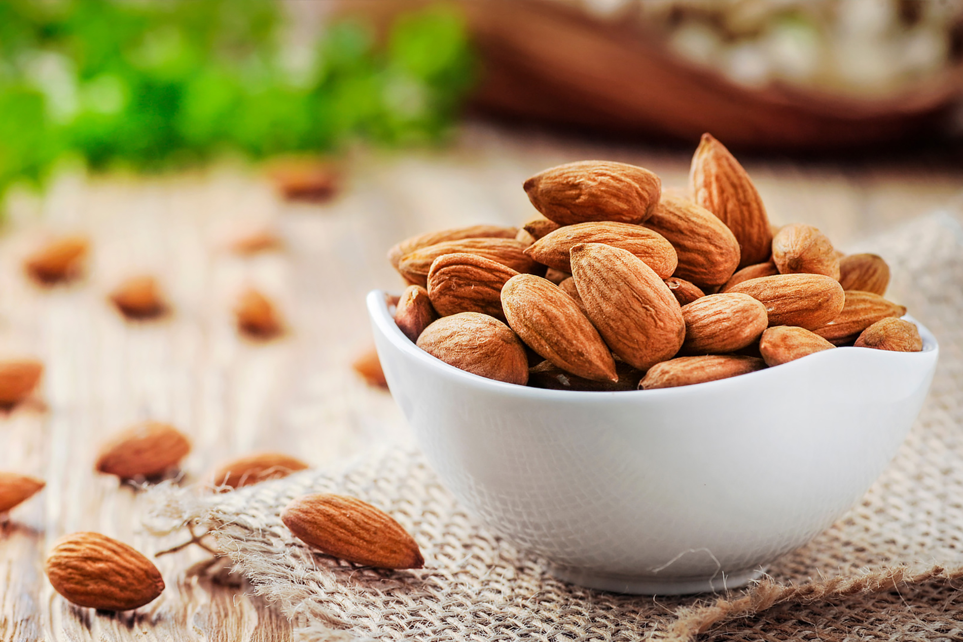 Bowl of almonds on table with scattered almonds next to bowl