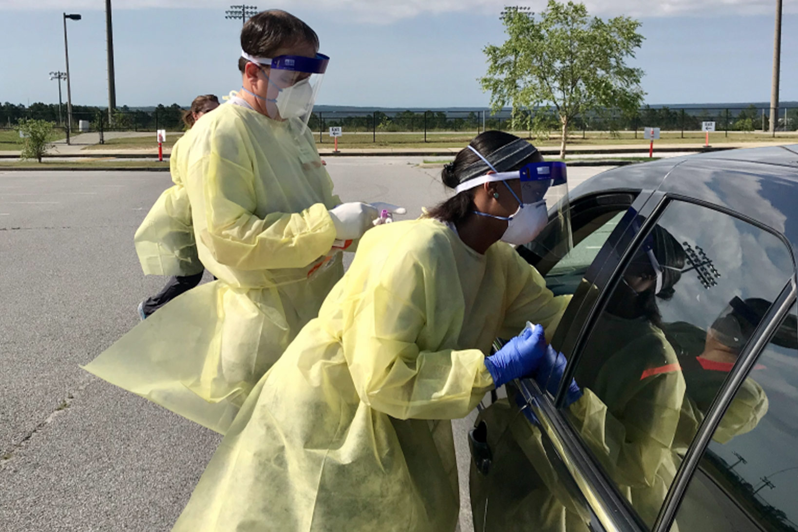 Clinicians in full protective gear and face shields in the Brookland Baptist Church parking lot give a COVID-19 test to a patient in a black sedan.