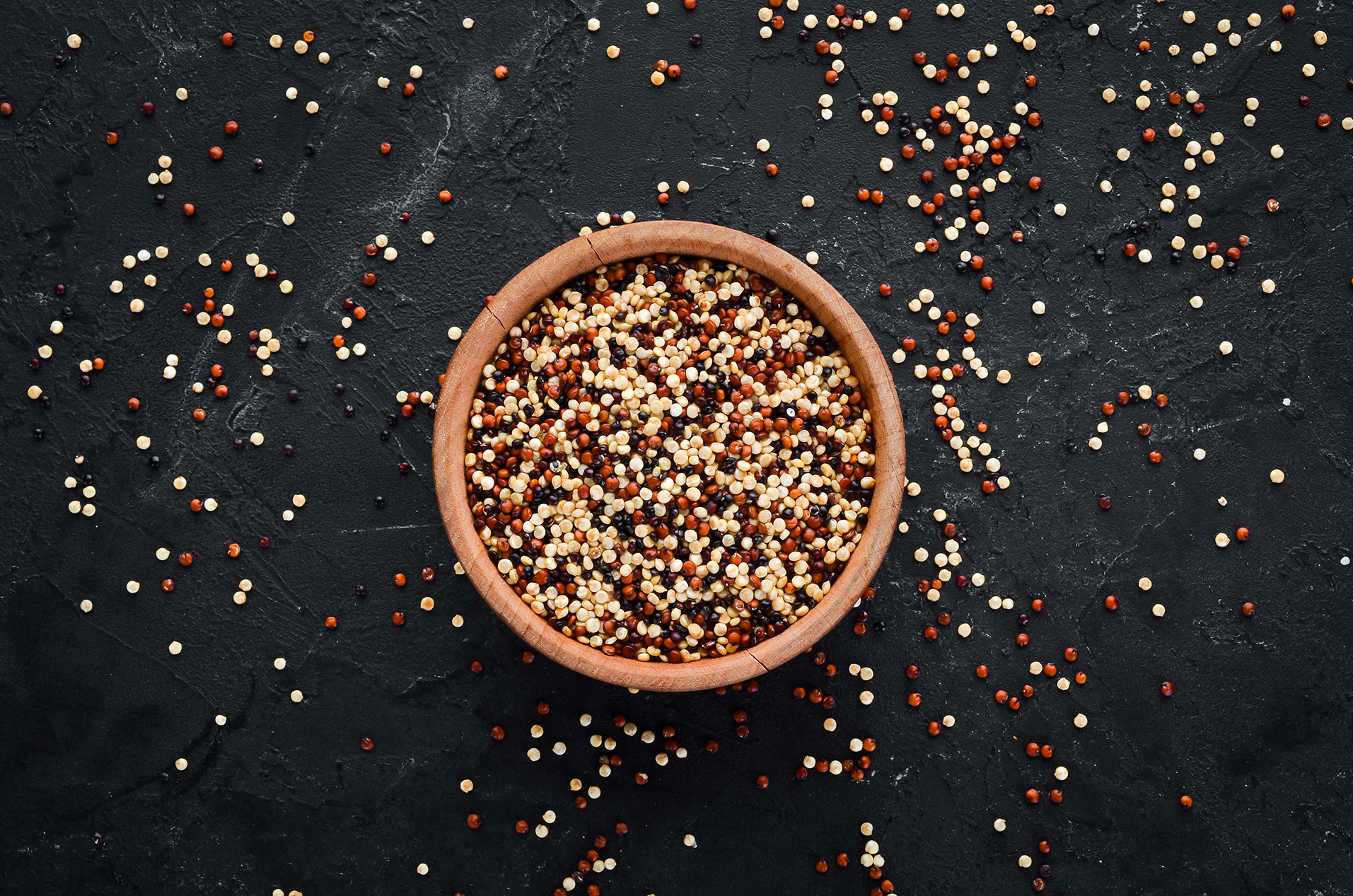 Red and white quinoa in wooden bowl on black granite counter