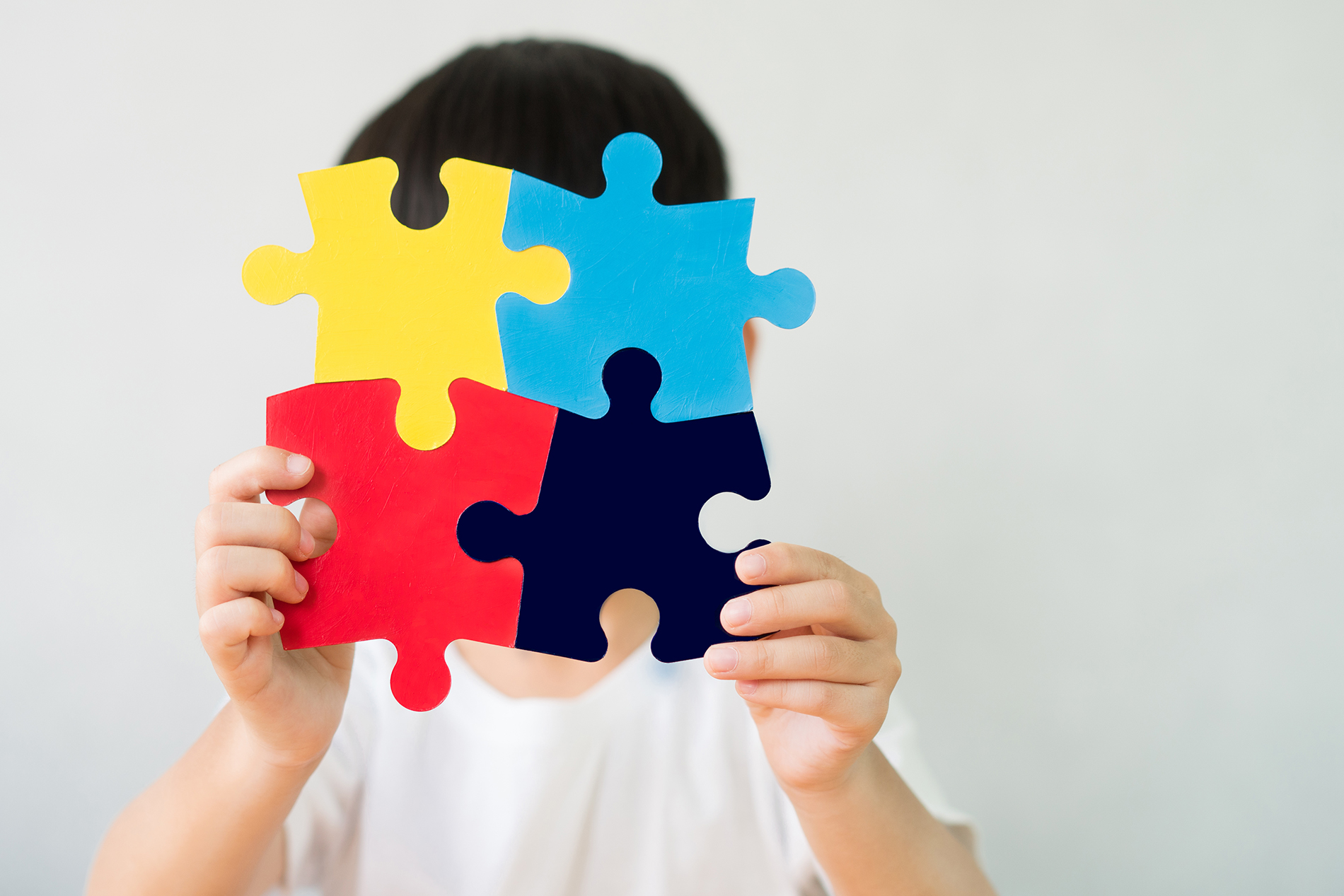 boy holding multi-colored puzzle pieces in front of his face