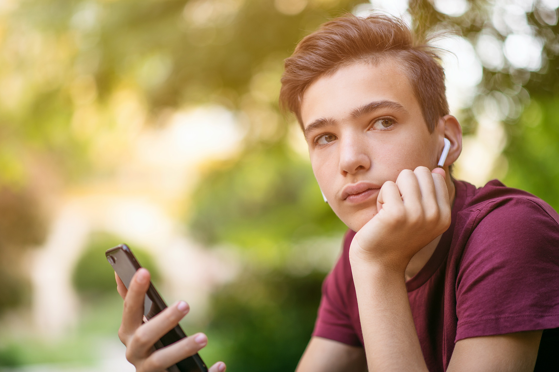 Pensive teenage boy sitting on bench with cell phone