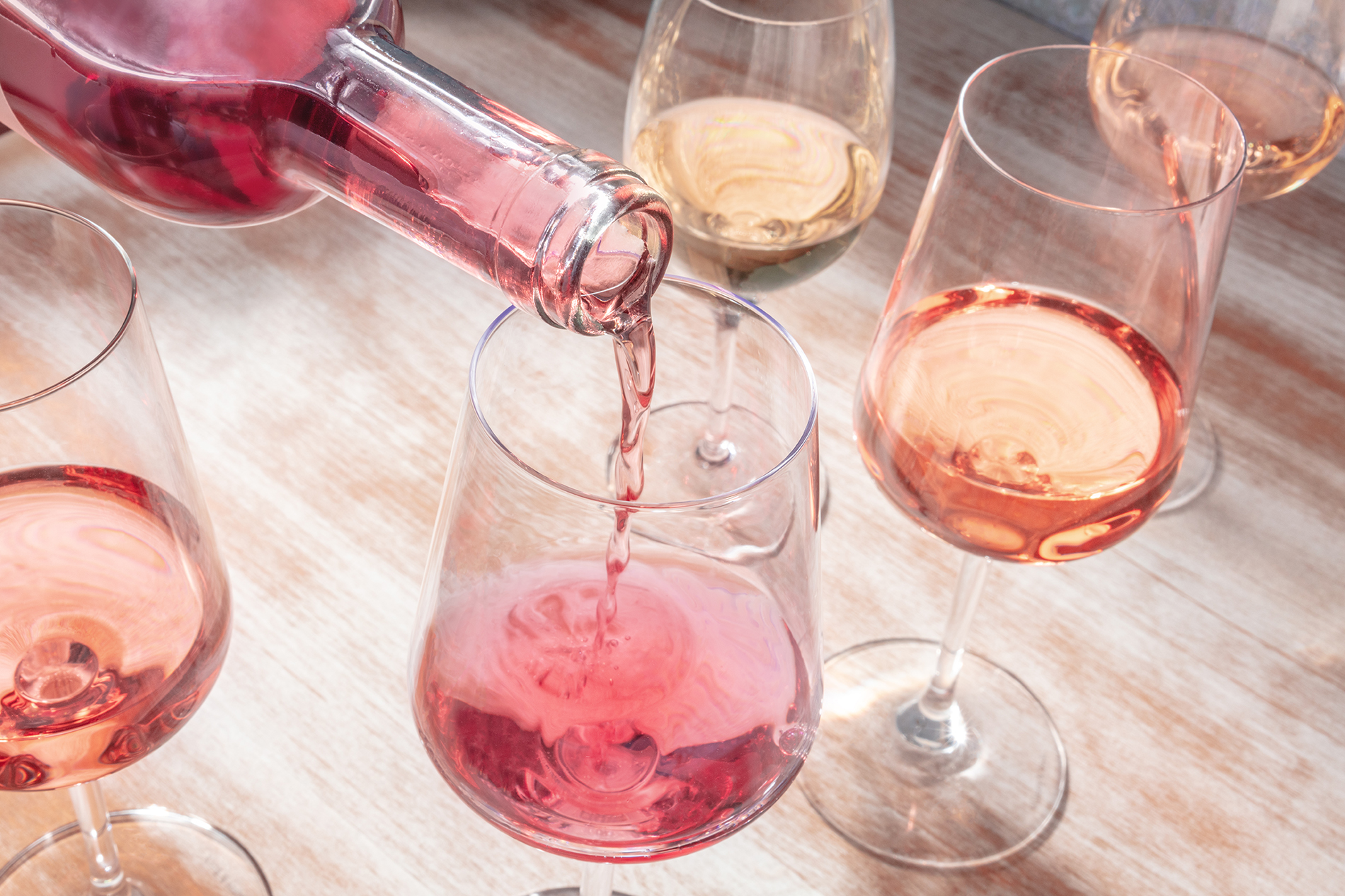 Hand pouring rose wine from bottle into multiple glasses