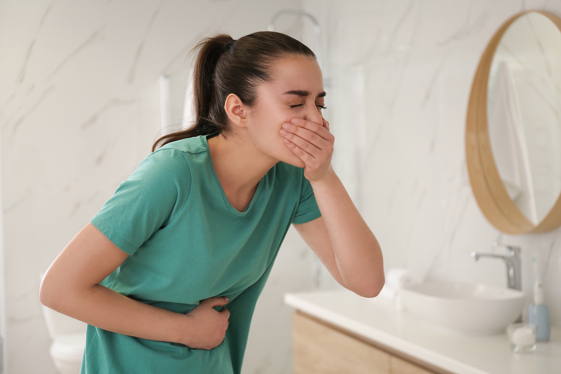 Young woman in bathroom with hand over mouth due to nausea