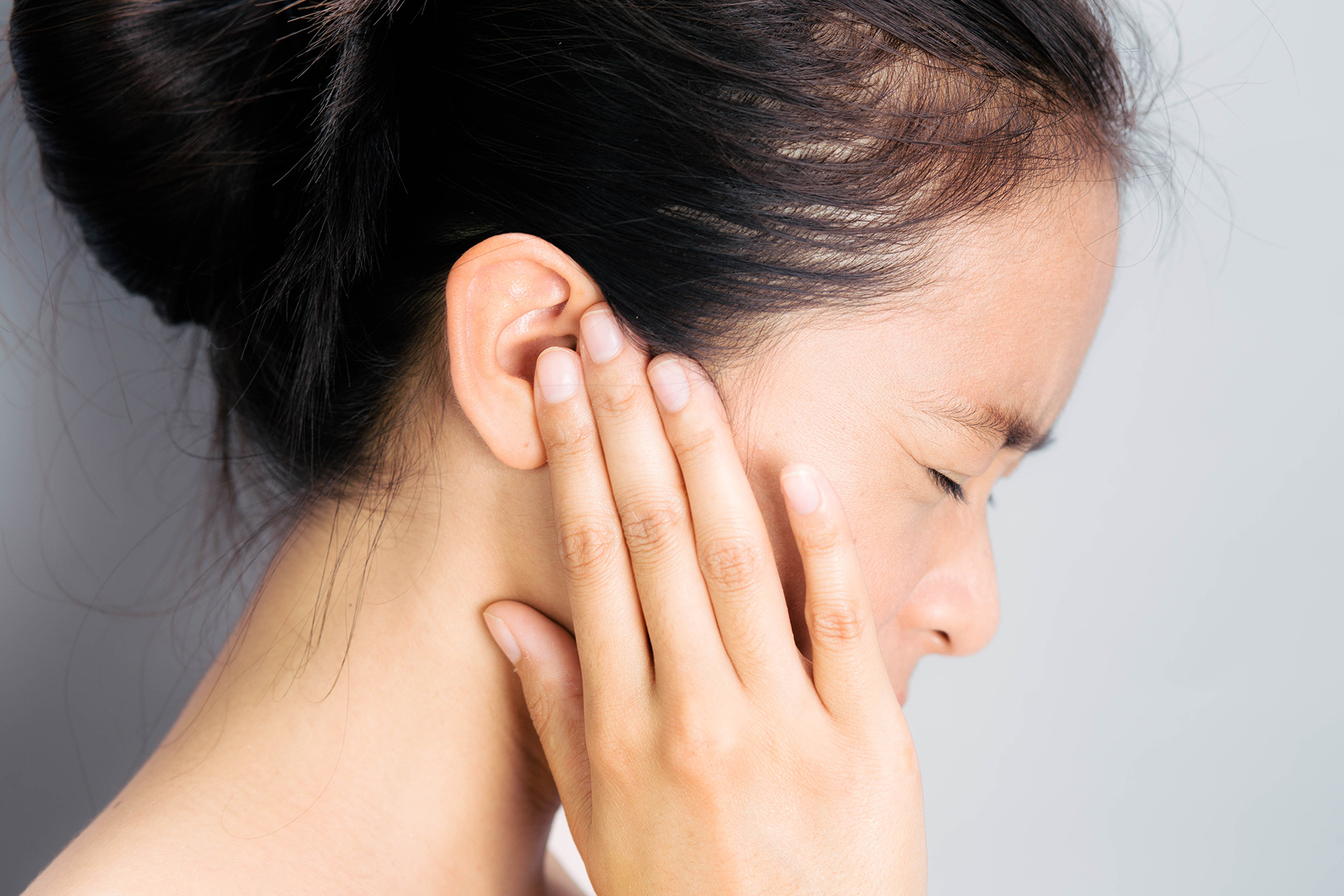 Asian woman in profile holding her hand at her ear in pain