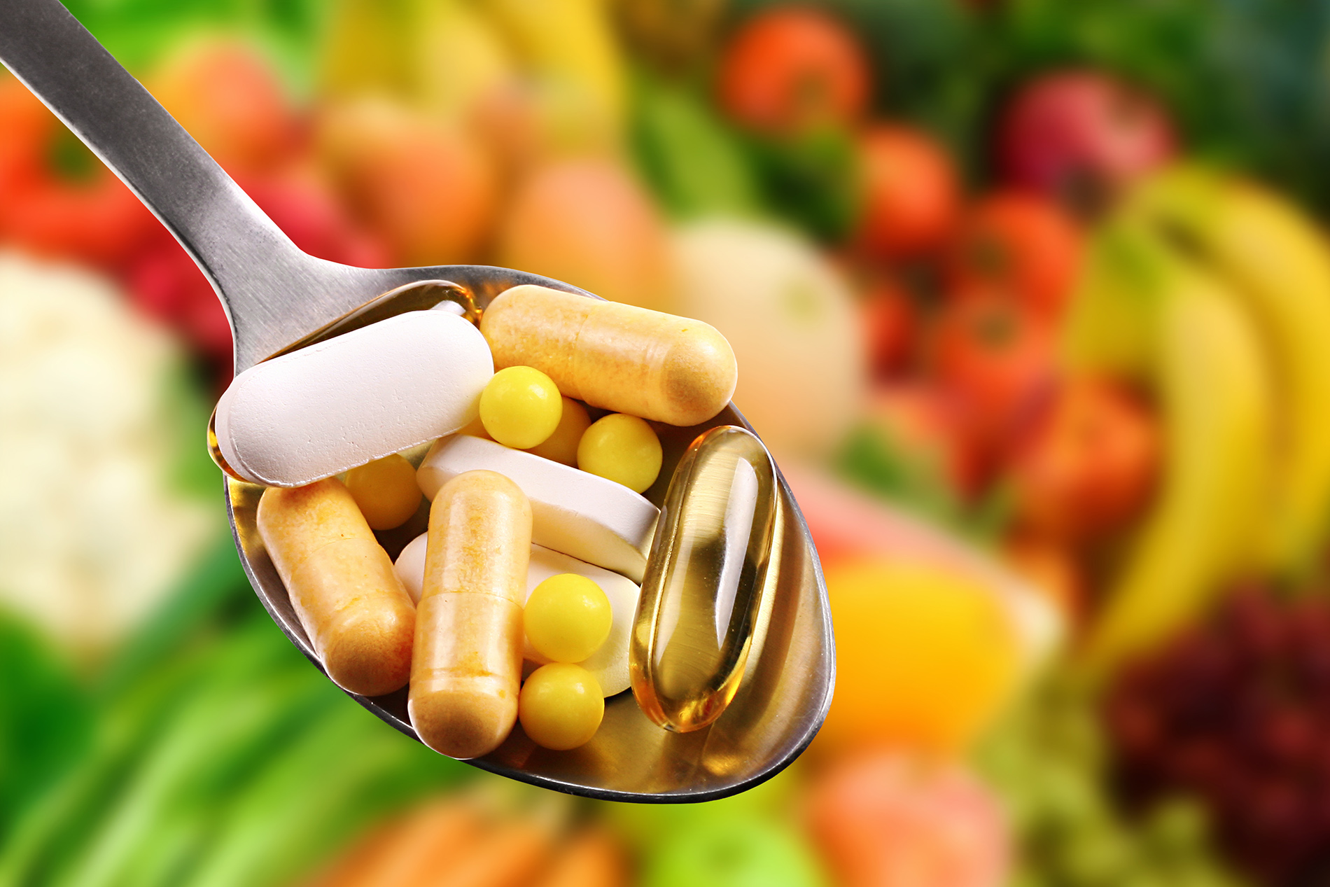 Spoonful of supplements with fruits and vegetables in the background