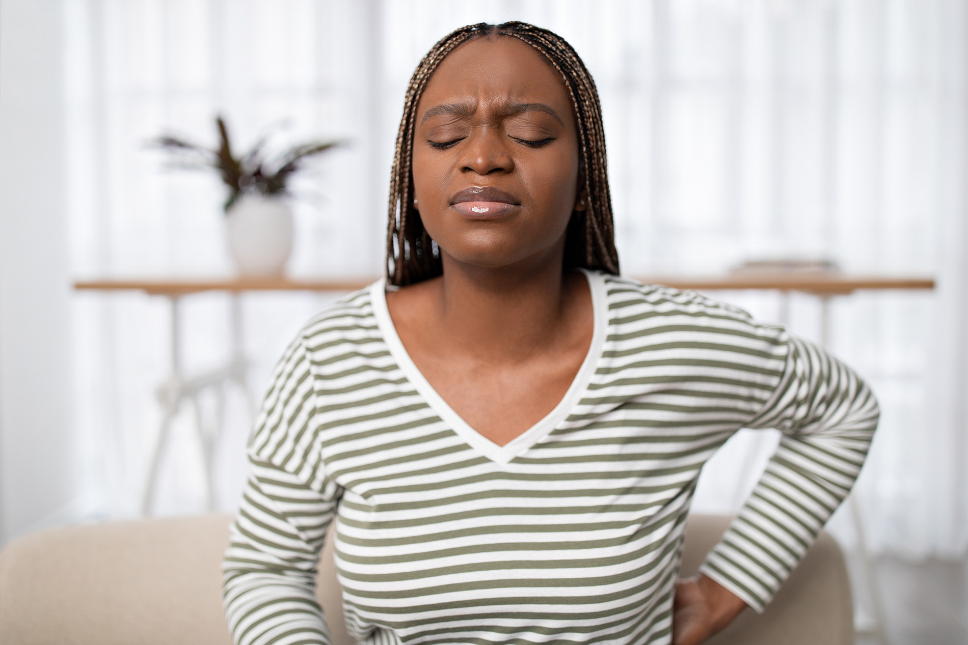 Black woman sitting on couch holding her lower back from kidney pain