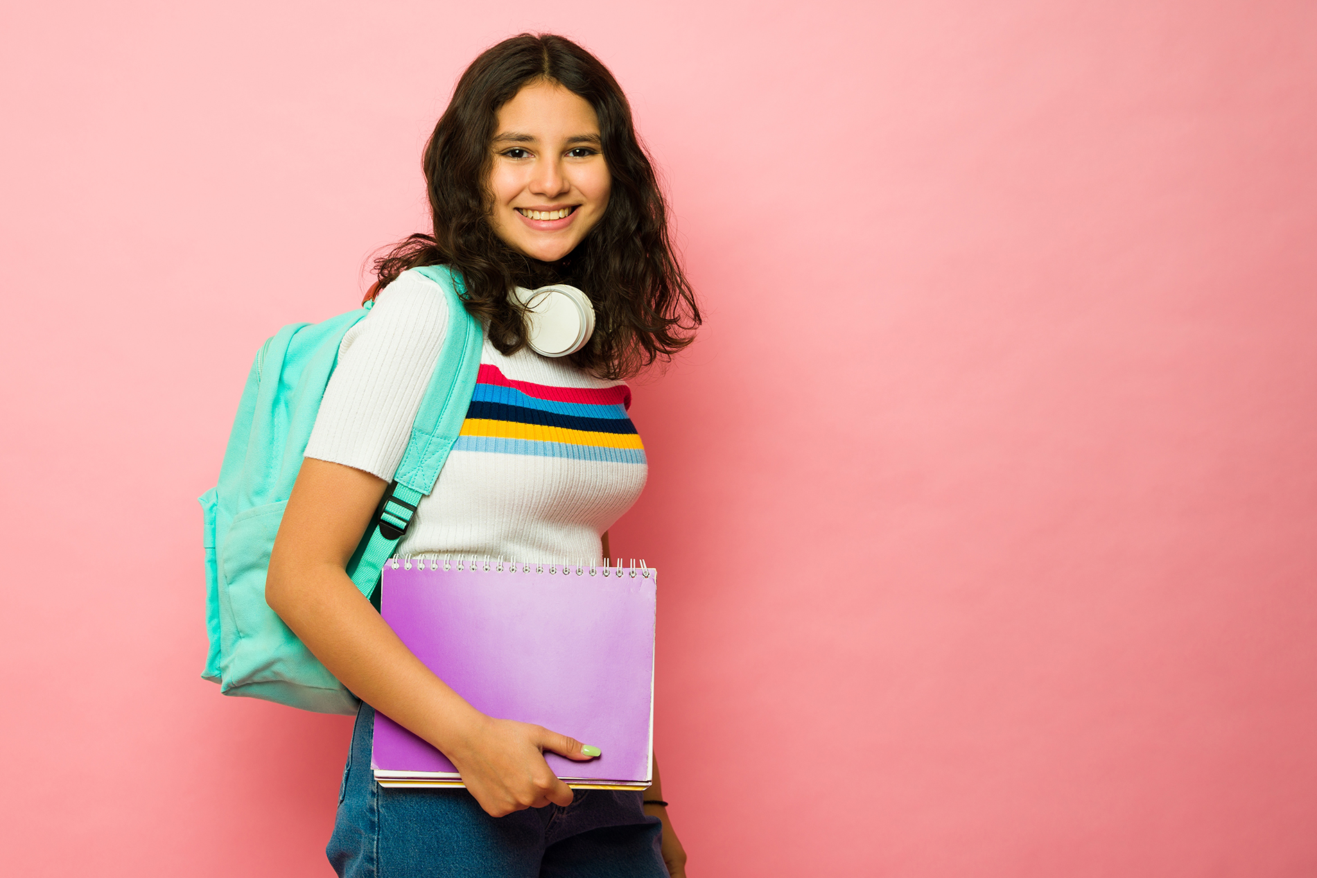 Teen girl with backpack and notebooks in front of pink background