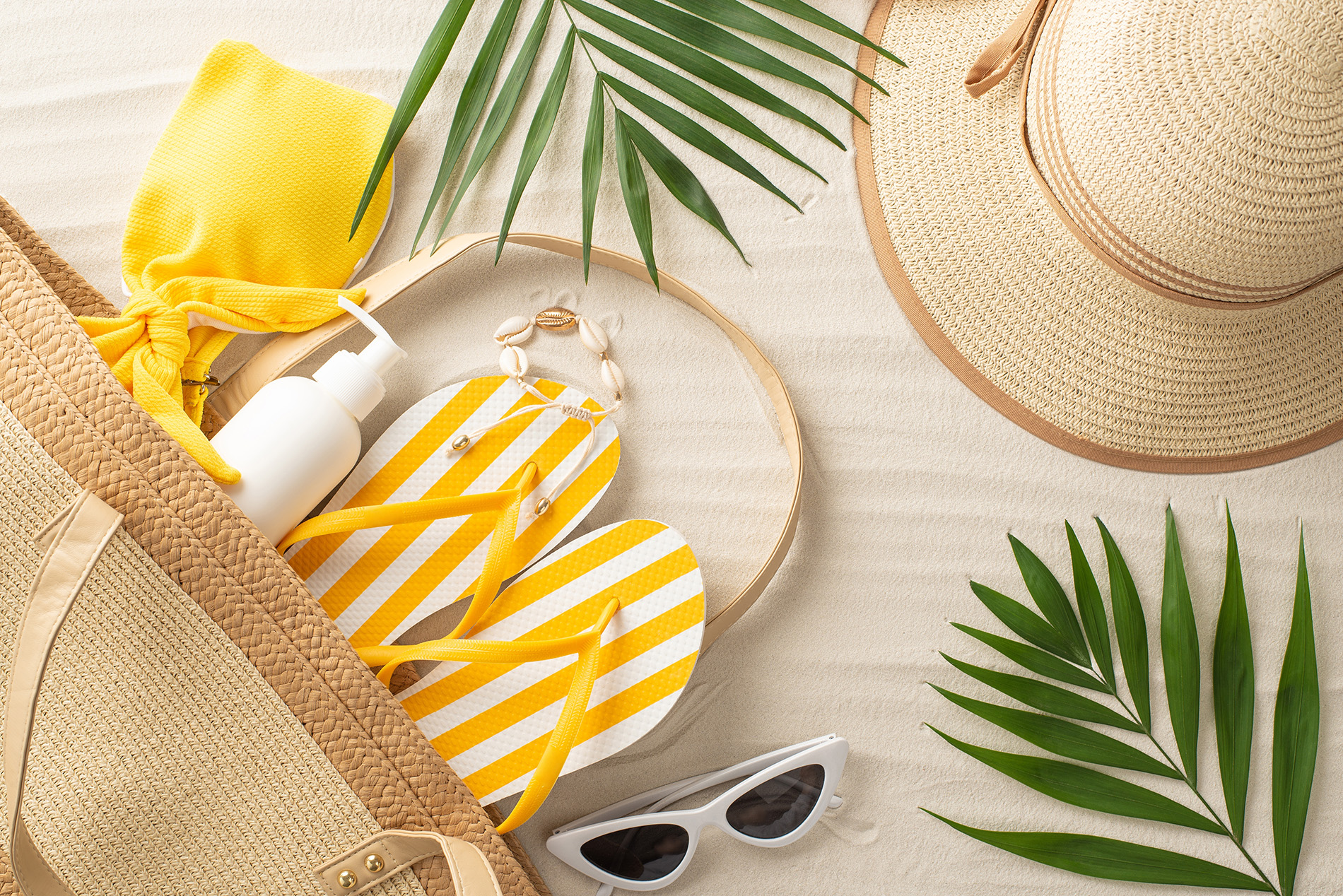Yellow and white flip flops, sunscreen and sunglasses in beach bag