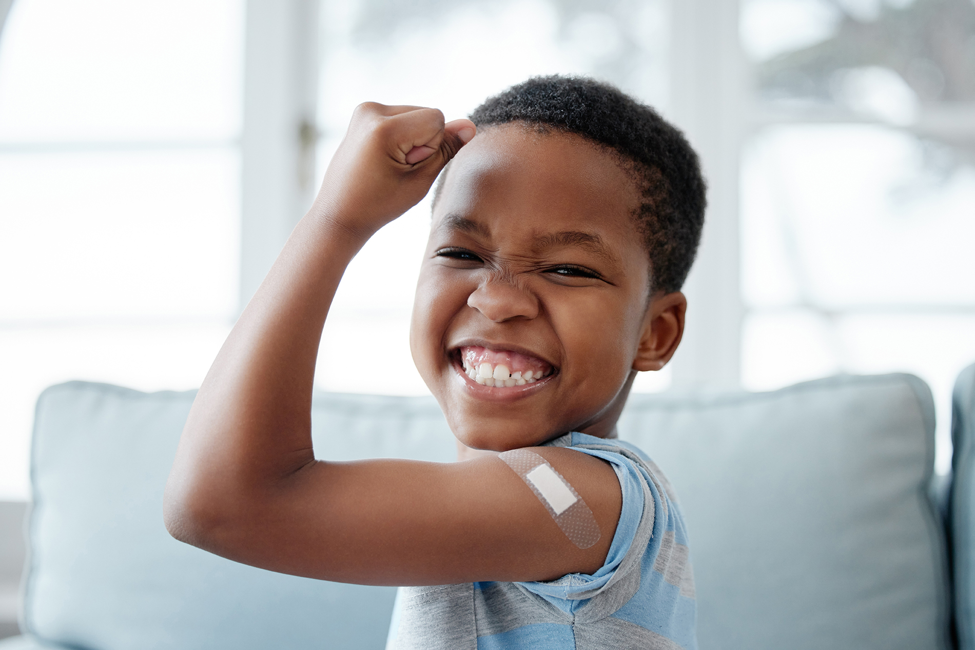 Black male child flexing his arm with a bandaid on his shoulder