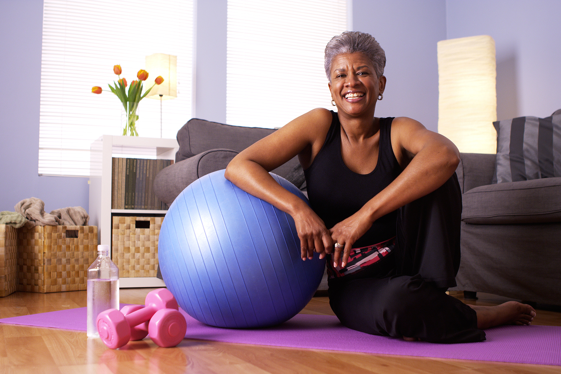 Black woman exercising at home with large ball and small weights