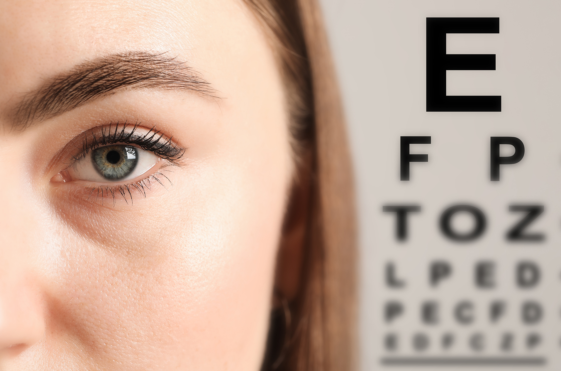 Close up of woman's blue eye with an eye exam chart in the background