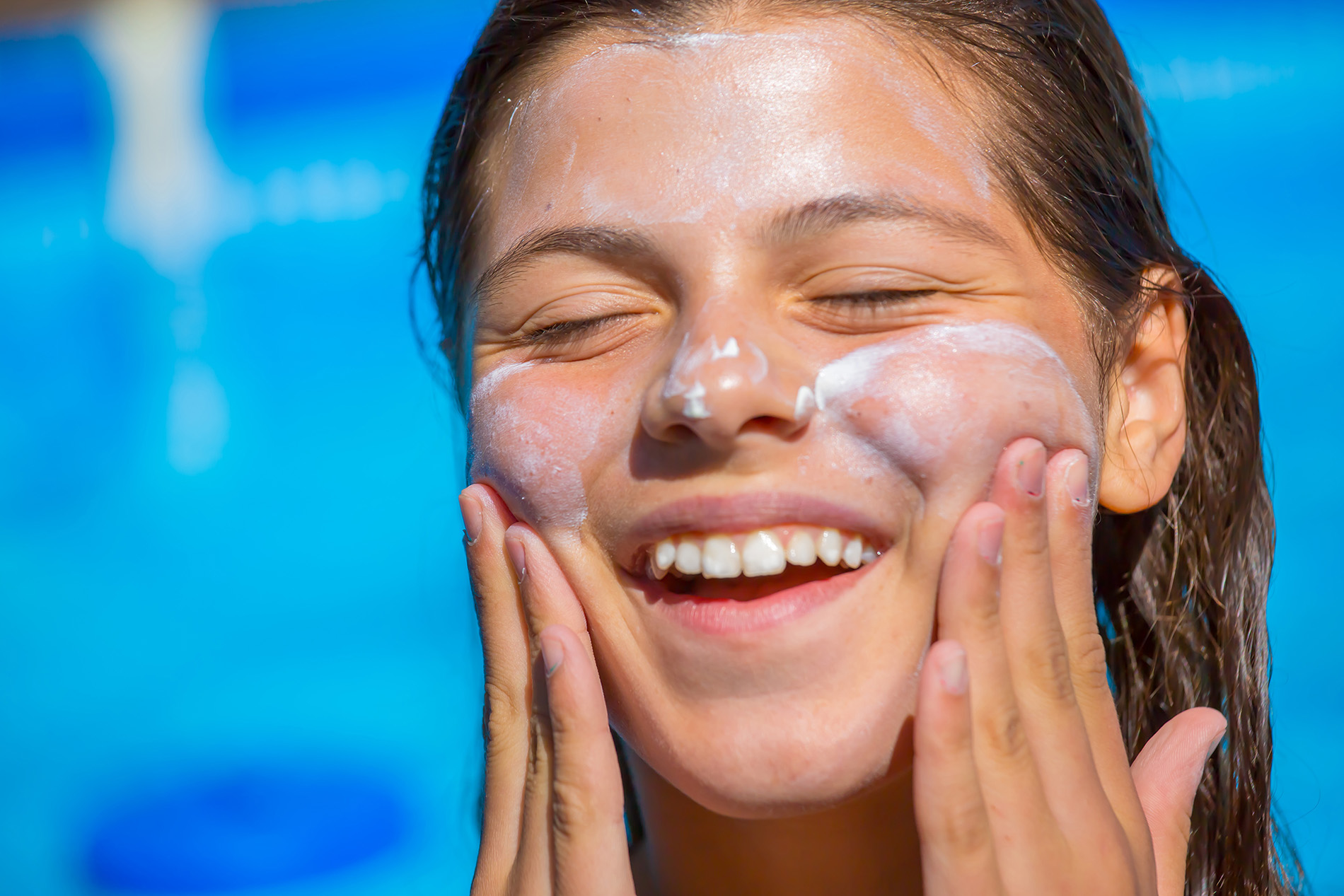 young girl applying sunscreen to face by pool