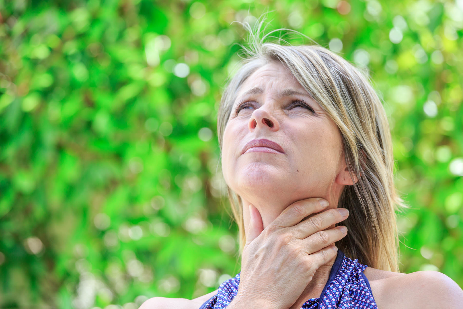 Woman outside touching her neck and looking upwards
