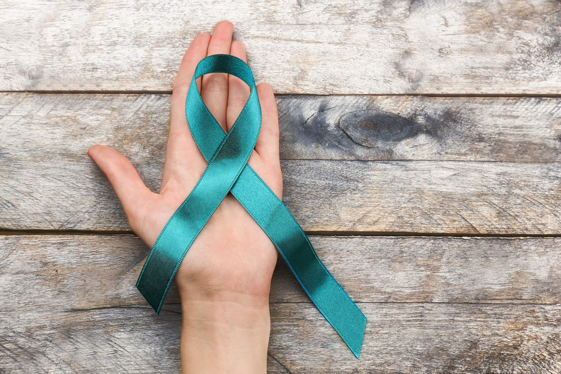 Woman's hand holding teal ribbon