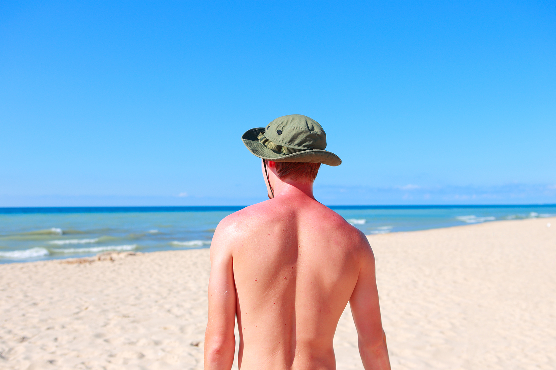 Man in hat on beach facing away from camera