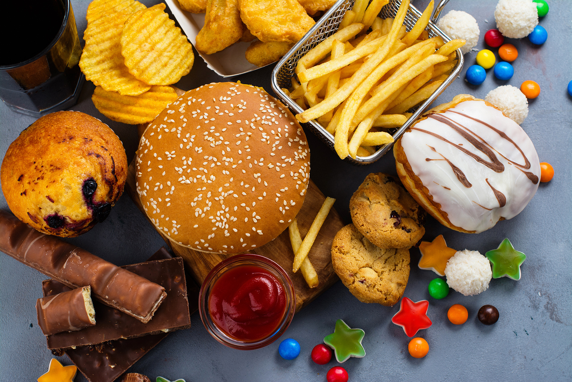 Array of ultra-processed foods, including doughnuts, candy, burger, nuggets, chips and a muffin