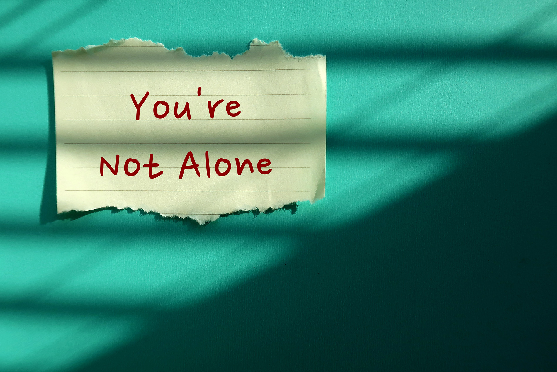 Sticky note on blue wall that says you're not alone.