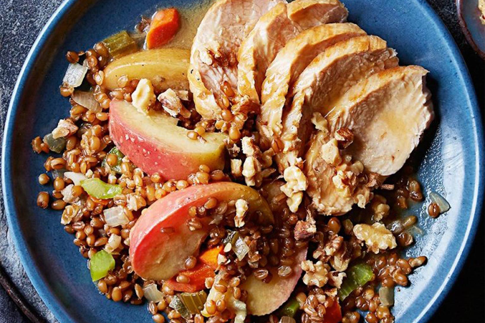 An apple salad with whole grains and walnuts on a blue plate.