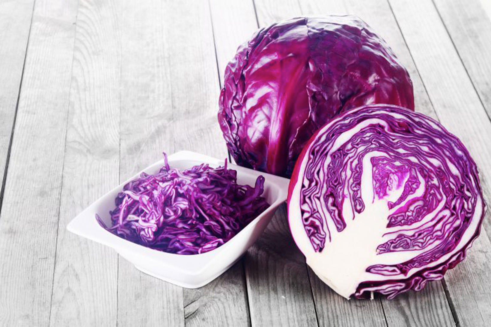 Red cabbage presented chopped in a white bowl, whole, and halved.