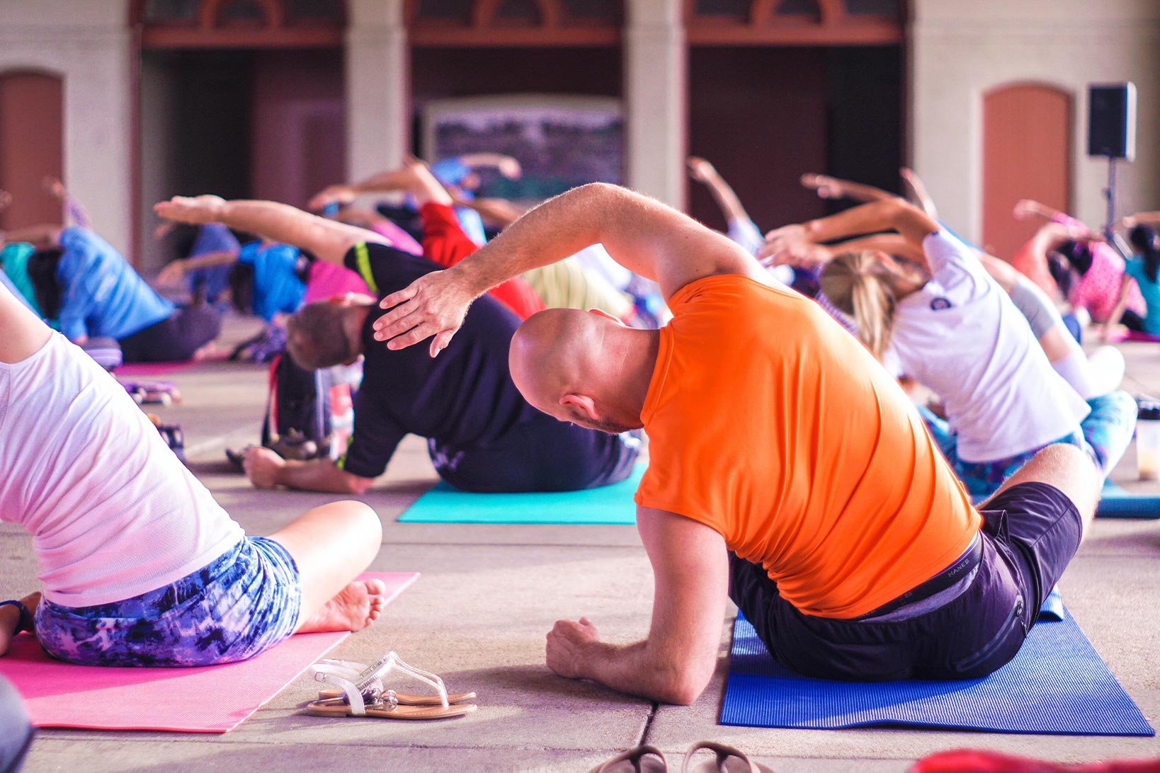 Participants in a yoga class sit in lotus position while bending to the left, their arms overhead.