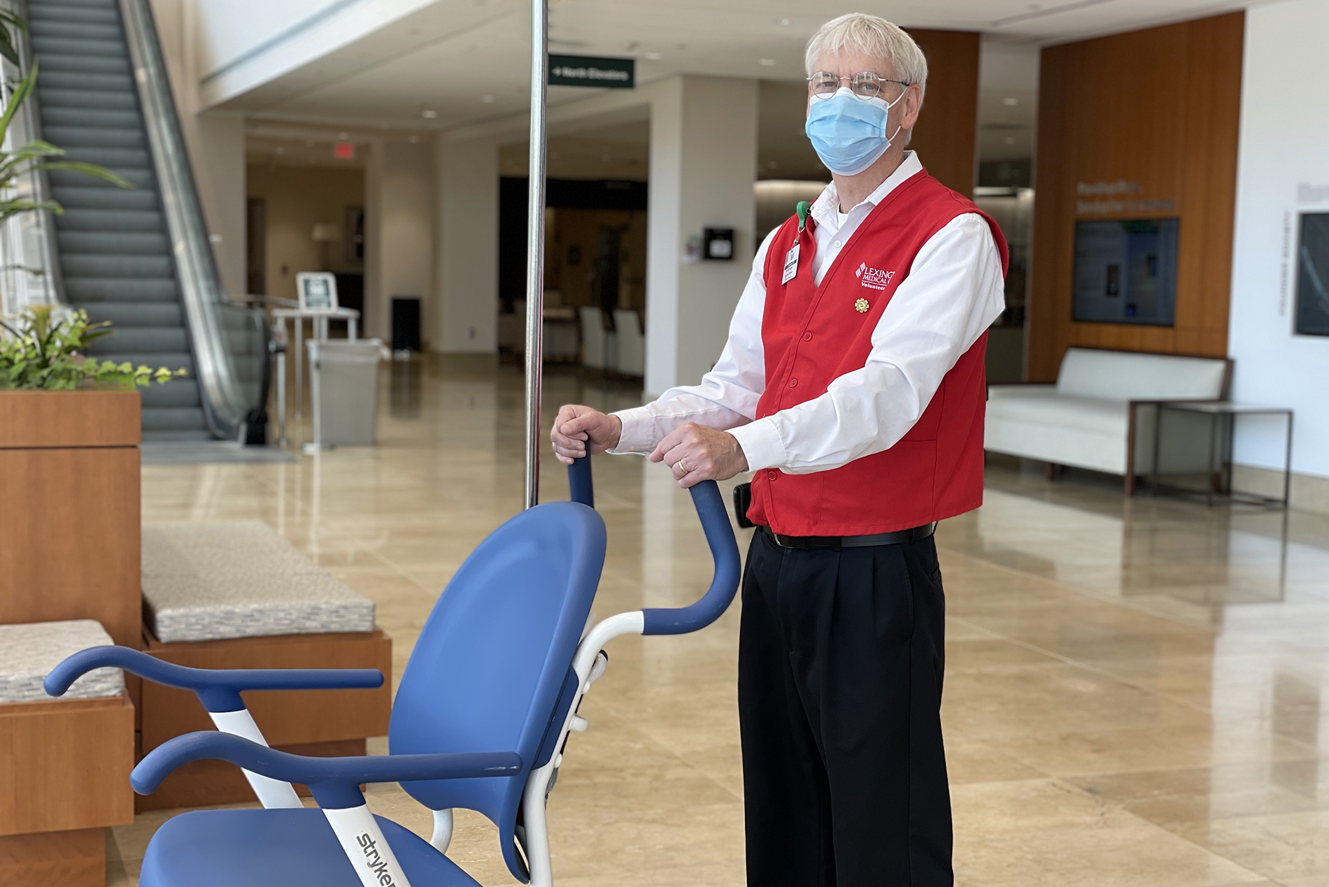 Male volunteer pushing wheelchair in hospital atrium
