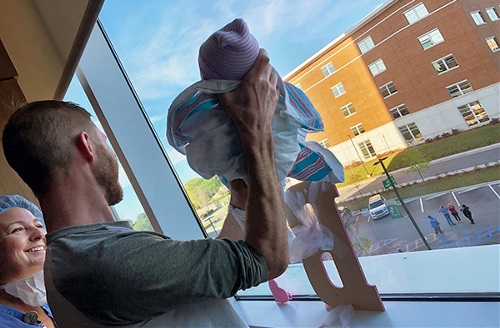 Father holding baby up to window for family outside 