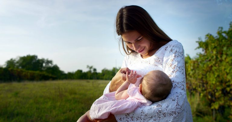 A mother holding her child in a green field on a sunny day.